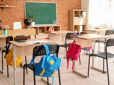 Empty classroom with childrens' backpacks slung on chairs